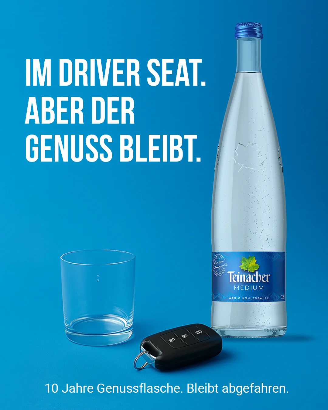Teinacher-Kampagnenmotiv 'Im Driver Seat – aber der Genuss bleibt': leeres Trinkglas und Autoschlüssel neben einer Flasche Teinacher Medium vor blauem Hintergrund