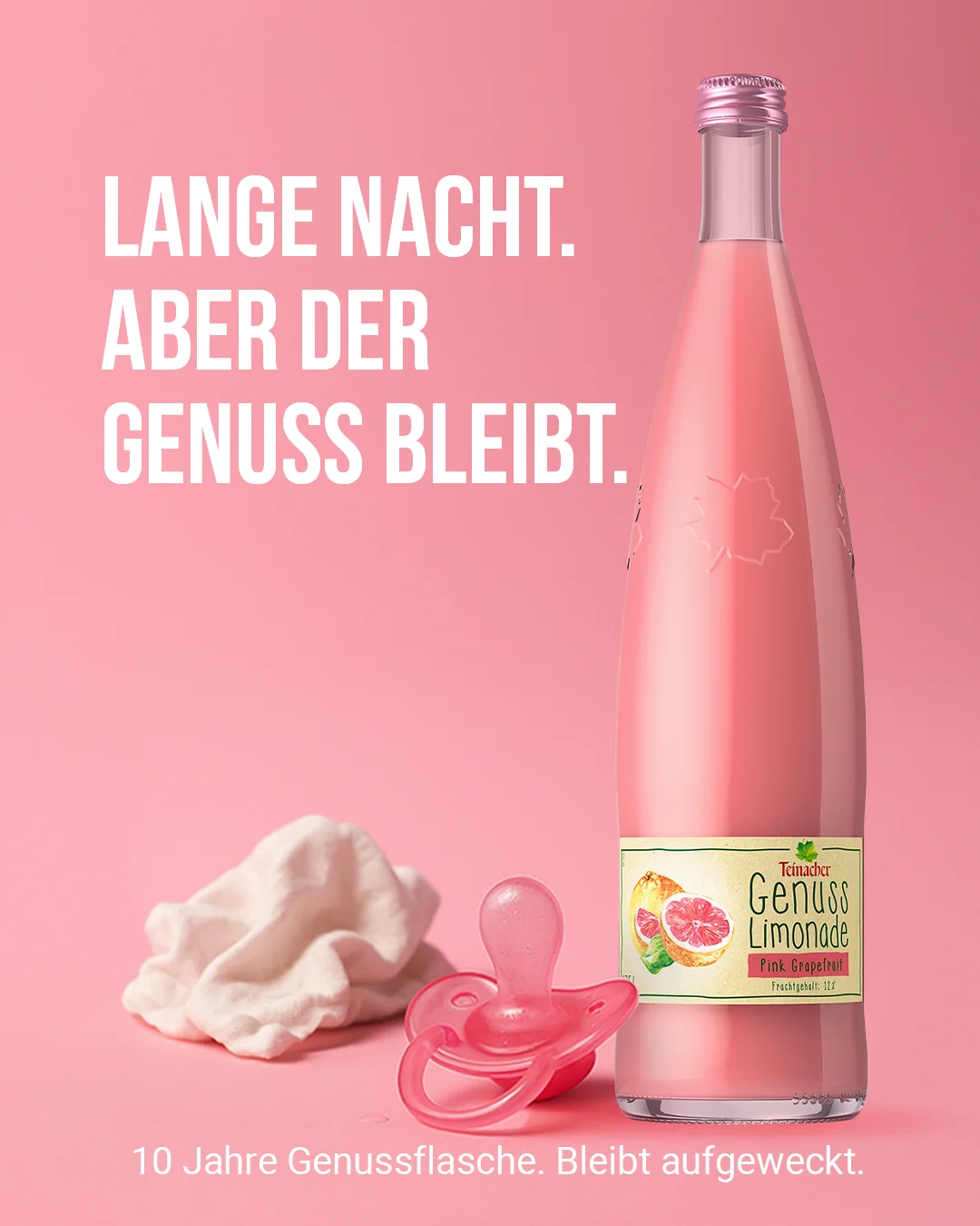 Teinacher-Kampagnenmotiv 'Lange Nacht – aber der Genuss bleibt': Stoffwindel und Schnuller neben einer Flasche Teinacher Genuss Limonade Pink Grapefruit vor rosa Hintergrund