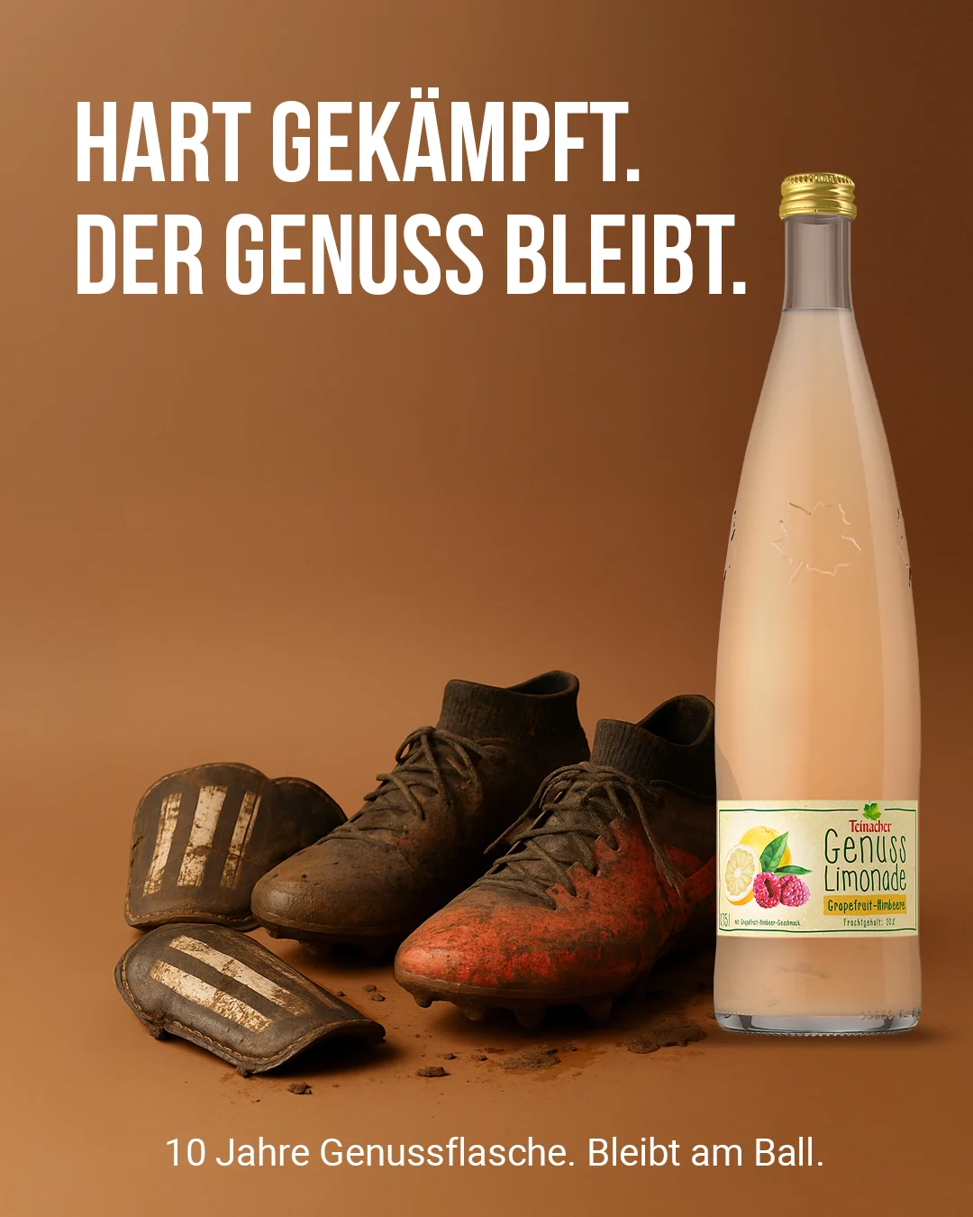 Teinacher-Kampagnenmotiv 'Hart gekämpft – der Genuss bleibt': schmutzige Fußballschuhe und Schienbeinschoner neben einer Flasche Teinacher Genuss Limonade Grapefruit-Himbeere vor braunem Hintergrund